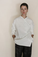 Load image into Gallery viewer, A person with short dark hair, wearing the Qipao Blouse | Cotton Omizarashi Undyed and dark pants, stands against a plain light background with hands in their pockets, looking directly at the camera.