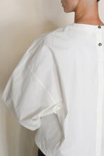 Load image into Gallery viewer, A person is seen from behind at an angle wearing the Cocoon | Cotton Omizarashi Undyed—a loose-fitting, handmade white shirt with large sleeves and two buttons on the upper back—crafted in San Francisco from Japanese textile.