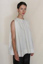 Load image into Gallery viewer, A woman with short dark hair wears the Shoulder Pleat Top | Omizarashi Undyed, a sleeveless white pleated cotton top handmade in San Francisco. She stands before a beige background, gazing calmly at the camera.