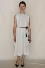 Load image into Gallery viewer, A woman with short hair and a neutral expression stands against a plain background, wearing the Shoulder Pleat Dress | Omizarashi Undyed with a black rope belt and black pointed-toe heels.