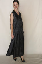 Load image into Gallery viewer, A person with short hair wears the V Neck Tank Reversible | Xiang Yun Silk Lingering Fragrance, a sleeveless black silk jacquard top, styled with a long black floral skirt and black pointed-toe heels, standing against a light beige background.