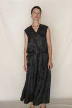 Load image into Gallery viewer, A person with short hair wears the Xiang Yun Silk Lingering Fragrance A Line Skirt, a black sleeveless V-neck dress with a subtle jacquard pattern, standing against a light beige background.
