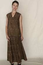 Load image into Gallery viewer, A woman with short dark hair wears the A Line Skirt | Xiang Yun Silk Lingering Fragrance, featuring a brown, sleeveless floral-patterned silk jacquard top and matching long skirt, standing against a plain beige background.