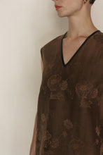 Load image into Gallery viewer, A person wears the V Neck Tank Reversible | Xiang Yun Silk Lingering Fragrance, a sleeveless brown silk jacquard top with a subtle floral pattern and black-trimmed V-neckline, shown from shoulders to mid-torso against a plain background.