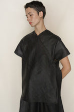 Load image into Gallery viewer, A person with short dark hair, gold hoop earrings, and red lipstick models the loose-fitting Qipao Vest Reversible in Xiang Yun Silk Faux Bois—black side out—standing against a plain light background with hands behind their back, looking down.