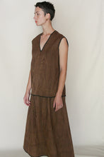 Load image into Gallery viewer, A person with short dark hair wears the A Line Skirt | Xiang Yun Silk Faux Bois, a sleeveless, loose-fitting brown skirt with black trim, posing against a plain light background and looking to the left.