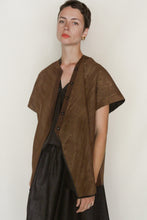 Load image into Gallery viewer, A person with short hair and gold earrings wears the Qipao Vest Reversible | Xiang Yun Silk Faux Bois in brown over a loose black top and skirt, standing against a plain light background.