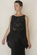 A person with short hair models the Uragiri Butterfly—a sleeveless, sheer black floral-patterned top—over a black skirt, standing with arms slightly extended against a plain light background.