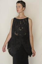 Load image into Gallery viewer, A person with short hair and gold earrings wears the Butterfly Silk Uragiri Black—a loose, sleeveless, sheer black floral top—over a black skirt, standing against a plain light background.