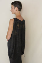 Load image into Gallery viewer, A person with short hair and gold hoop earrings stands sideways, wearing a loose, sleeveless Butterfly| Silk Uragiri Black top with a draped back, against a plain light background.