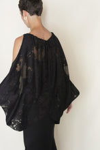 Load image into Gallery viewer, A person with short hair wears the Butterfly | Silk Uragiri Black top and a black skirt, standing against a plain light background, facing partially away from the camera with one arm extended.