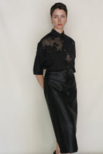 Load image into Gallery viewer, A person with short hair and a neutral expression stands against a plain background, wearing a black sheer floral blouse and the high-waisted, handmade Futo Skirt | Xiang Yun Silk Earth Mark, featuring a unique crackled surface.