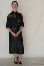 Load image into Gallery viewer, A person stands against a plain backdrop, wearing a sheer black floral blouse, the Futo Skirt | Xiang Yun Silk Earth Mark, and black heels. Their hands are clasped in front as they look directly at the camera.