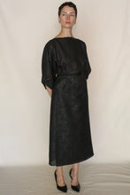 Load image into Gallery viewer, A person with short hair stands against a plain backdrop, wearing a loose-fitting, knee-length black dress and black heels, effortlessly styled with the Reversible Futo Skirt in elegant Xiang Yun Silk Endless Bloom.