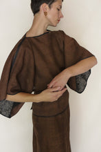 Load image into Gallery viewer, A person with short hair models the Kimono Top Reversible | Xiang Yun Silk Endless Bloom, a loose brown kimono with wide sleeves and black lace trim inside the reversible silk sleeves, standing against a plain backdrop with arms gracefully posed.