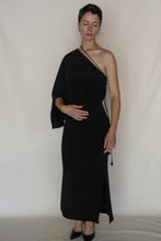Load image into Gallery viewer, A woman stands against a plain background wearing the Eurie Skirt in 2 Ply Silk Crepe Black, styled with black heels. She gazes slightly downward with one hand on her waist, highlighting the skirt's elegant mid-calf silhouette.