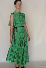 Load image into Gallery viewer, A person wearing the Hand Pleated Column Dress Hidden Peony Emerald stands against a plain light background, eyes closed, arms relaxed at their sides.
