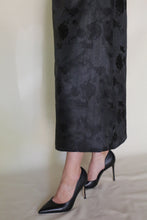 Load image into Gallery viewer, Someone stands on a light surface against a neutral background wearing the Reversible Futo Skirt | Xiang Yun Silk Lingering Fragrance, a dark jacquard floral silk skirt, paired with black pointed-toe high heels.