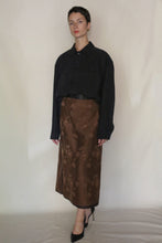 Load image into Gallery viewer, A person with short hair and a neutral expression stands against a plain background wearing the Men's Shirt | Xiang Yun Silk Earth Mark in black, paired with a brown floral midi skirt and black heels.