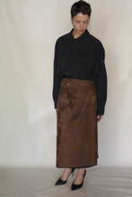 Load image into Gallery viewer, A person with short hair wears a loose black button-up shirt tucked into the Reversible Futo Skirt | Xiang Yun Silk Lingering Fragrance and black pointed-toe heels, standing against a plain light background and looking down.
