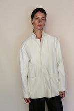 Load image into Gallery viewer, A person with short dark hair wears the Painter's Jacket | Cotton Serge Ivory, featuring large front pockets, standing against a plain beige background and looking directly at the camera with a neutral expression.
