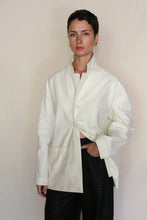 Load image into Gallery viewer, A person with short dark hair, wearing the Painter's Jacket | Cotton Serge Ivory and black pants, stands against a plain light background with one hand in their pocket.