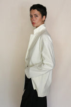 Load image into Gallery viewer, A person with short dark hair stands sideways, one hand in their pocket, wearing the Painter's Jacket | Cotton Serge Ivory and dark pants against a plain light background.
