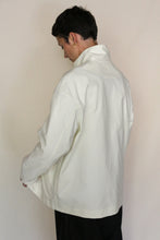 Load image into Gallery viewer, Wearing the Painter's Jacket | Cotton Serge Ivory, a person with short dark hair and gold hoop earrings stands facing away from the camera against a plain, light background.