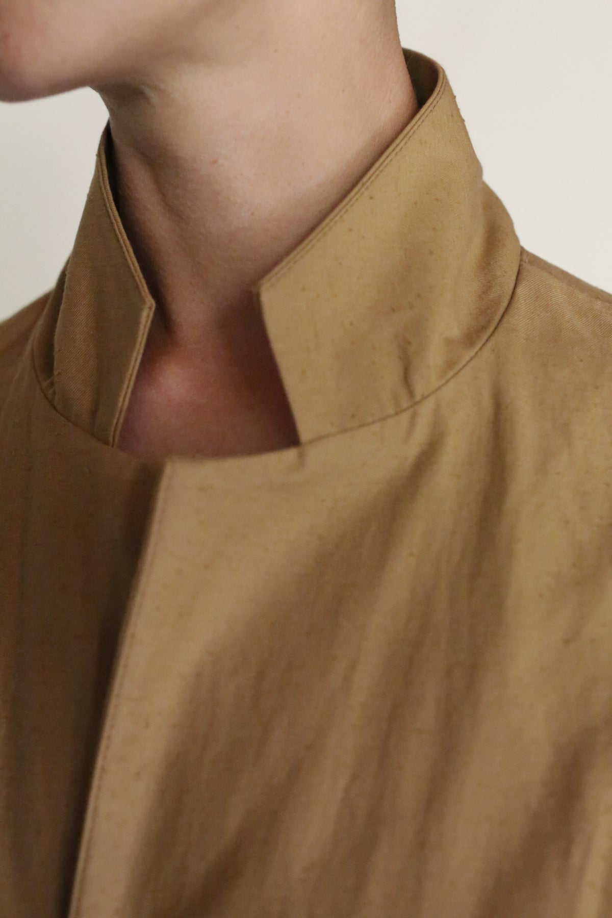Close-up of a person wearing the Painter's Jacket | Tan, featuring a high collar and slightly open neckline. The focus is on the neck and upper chest, showcasing the textured cotton serge and minimalist, handmade San Francisco style.