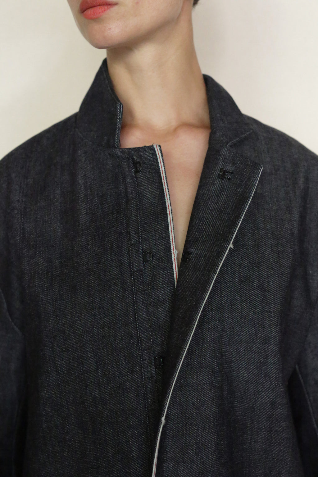 A person wears the Painter's Jacket | Japanese Selvedge Denim with an open collar and no fastened buttons, revealing part of their neck and jawline against a plain background.