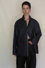 Load image into Gallery viewer, A person with short dark hair stands against a plain background, wearing the Painter's Jacket | Japanese Selvedge Denim over matching wide-leg pants, one hand in a pocket and a calm expression.