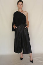 Load image into Gallery viewer, A person poses confidently with hands in pockets, wearing a black one-shoulder top, Samurai Pants | Xiang Yun Silk Lingering Fragrance in black jacquard, and black heels against a plain background.