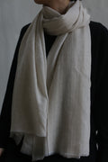 A person wearing a black top is shown from the shoulders down, with a Tissue Weight Cashmere Scarf in Oat, measuring 36" x 82", wrapped around their neck. The scarf drapes elegantly over their chest, contrasting beautifully with the dark garment. The background is neutral.