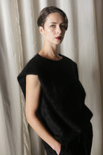 Load image into Gallery viewer, A person with short hair stands before a light curtain, wearing the Salento | Black vest over a sleeveless black top. They wear dark lipstick and maintain a neutral expression, with their left hand casually in their pocket.