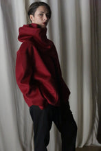 Load image into Gallery viewer, A person with short hair poses in a wine-colored Bamford Short Double-Face Cashmere coat featuring a high collar and black pants, standing in front of white curtains. The modern fit enhances their contemporary wardrobe style, while the dim lighting creates a moody atmosphere.