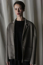 Load image into Gallery viewer, A person with short dark hair wearing the Bamford Short Double-Face Cashmere in Undyed Natural stands in front of a plain background. The luxurious coat features large pockets and buttons. Their expression is neutral, while the soft and dim lighting enhances the elegance of this contemporary wardrobe choice.