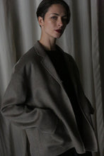 Load image into Gallery viewer, A person with short hair wears the Bamford Short Double-Face Cashmere jacket in a dark, oversized style from a contemporary wardrobe, posing in front of a curtain. The low lighting casts shadows on their face and background, enhancing the modern aura of the scene.