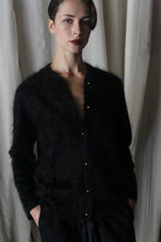 Load image into Gallery viewer, Against a light curtain background, a person with short, sleek hair poses with hands in pockets, wearing a dark Brushed Cashmere Cardigan and matching pants, looking directly at the camera.