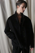 Load image into Gallery viewer, Wearing the Bamford Short Double-Face Cashmere coat in black, a person with short hair stands against a gently draped white curtain. Their eyes are closed and posture relaxed, with one hand in their pocket, perfectly capturing the serene essence of this contemporary wardrobe essential.