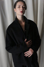 Load image into Gallery viewer, A person elegantly poses in front of light-colored curtains, wearing the Bamford Short Double-Face Cashmere coat in black. One hand gently holds the coat closed while the other rests near the waist, capturing the essence of a contemporary wardrobe essential.