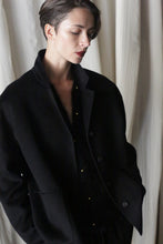 Load image into Gallery viewer, Clad in a must-have modern wardrobe piece—the Bamford Short Double-Face Cashmere in Black—a person stands against a delicately textured backdrop. With their head gently inclined downward and hands nestled into the opulent double-faced cashmere pockets, they embody a contemplative yet relaxed stance.