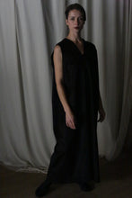 Load image into Gallery viewer, A person stands in a dimly lit room wearing The Winter Dress in black cashmere. The background features draped white curtains, adding to the serene atmosphere.