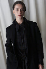 Load image into Gallery viewer, A person with short hair is wearing the Unisex Blazer Double-Face Cashmere in Charcoal over a plaid shirt. They stand against a white curtain backdrop, looking into the camera with a serious expression.