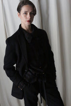 Load image into Gallery viewer, A person with short hair is wearing a charcoal Unisex Blazer Double-Face Cashmere and standing against a white curtain backdrop. They have their hands in their pockets and are looking towards the camera with a neutral expression.