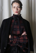 Load image into Gallery viewer, A person with short hair stands before a curtain, wearing a Simple Shirt in Japanese Wool Gauze Wine Plaid with black ribbons and gold pins, under a black jacket. Embracing Lan Jaenicke classics, they have a neutral expression and arms crossed.