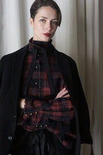 Load image into Gallery viewer, A confident person with short dark hair wears the Simple Shirt in Japanese Wool Gauze Wine Plaid, paired with black straps under a Lan Jaenicke dark jacket, set against softly lit light-colored curtains.