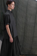 Load image into Gallery viewer, A woman with short brown hair stands in profile, wearing the Work Shirt | Typewriter Cotton Black. She is in front of a dark, semi-transparent fabric backdrop.