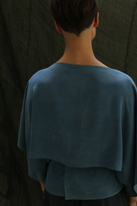 A person with short dark hair is shown from behind, wearing the Kimono Top | 2-ply Silk Crepe Ai Dye in blue. The loose fit and textured silk stand out against a softly contrasting dark background.