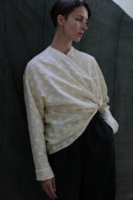 Load image into Gallery viewer, A person with short dark hair wears the Qipao Blouse | Polkadot Seersucker Butter and loose black pants, standing against a dark green fabric background.
