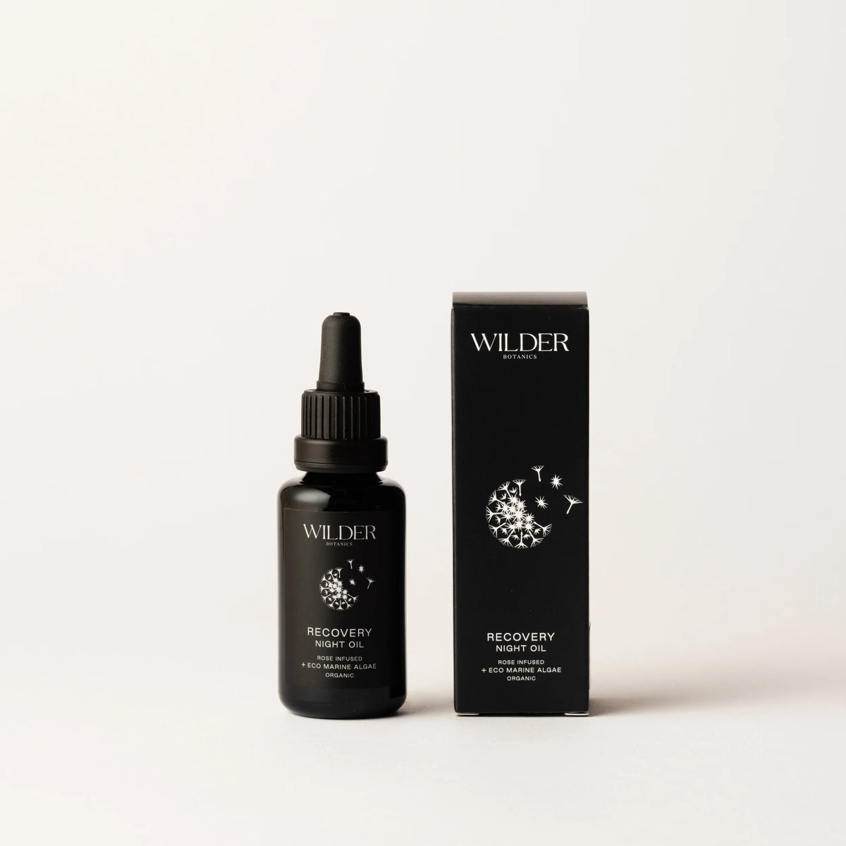 A black dropper bottle labeled "Recovery Night Oil" stands alongside its matching box, both adorned with a white crescent moon and dandelion design, emphasizing its organic night oil blend. A soothing light gray serves as the backdrop.